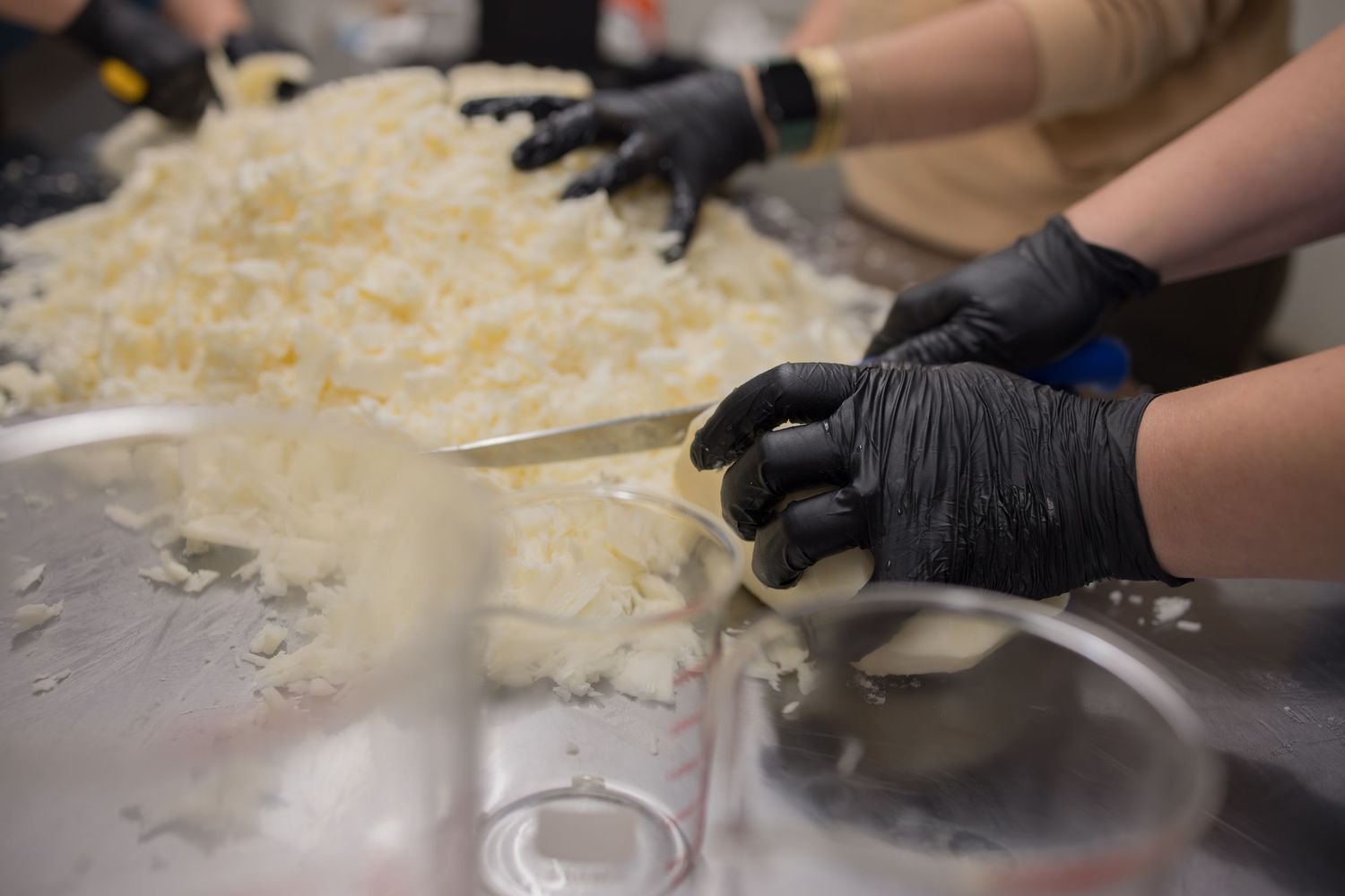 Hands wearing black gloves prepare ingredients on a stainless steel surface with shredded food visible.