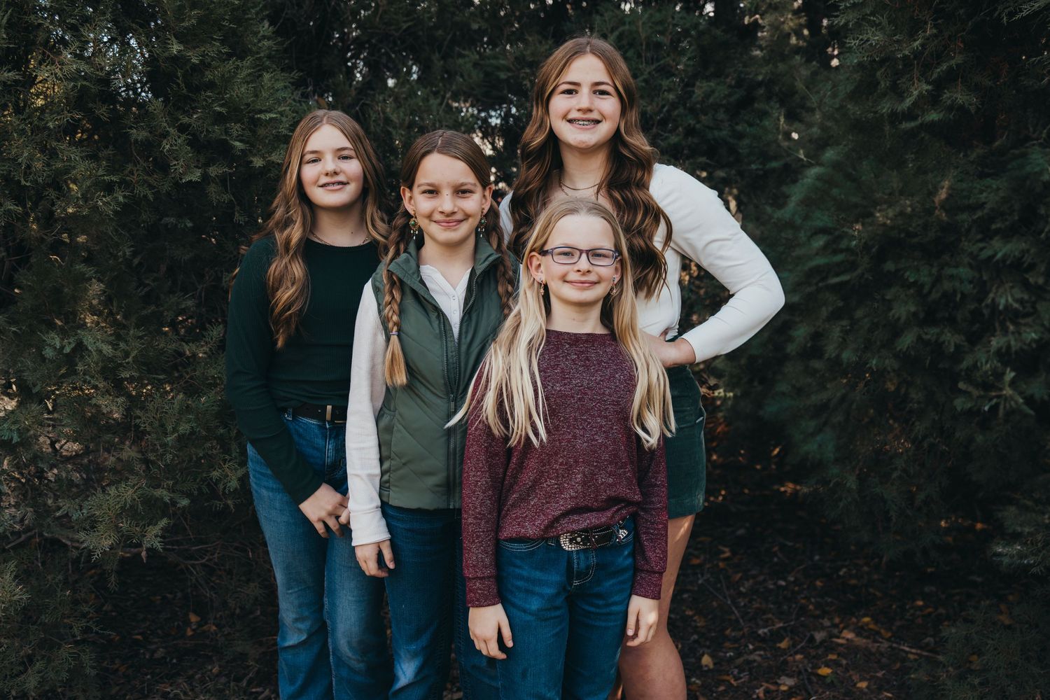 Four young people in casual clothing stand together against a dark forest background.