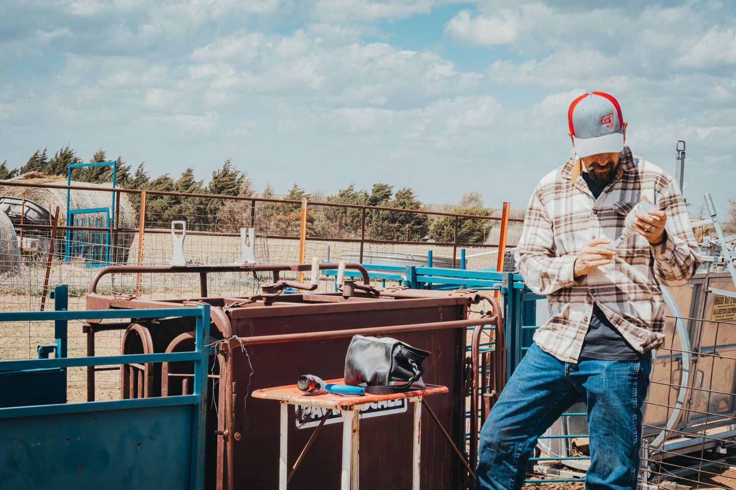 Ranch worker in plaid shirt and cap working with equipment in an outdoor livestock facility.