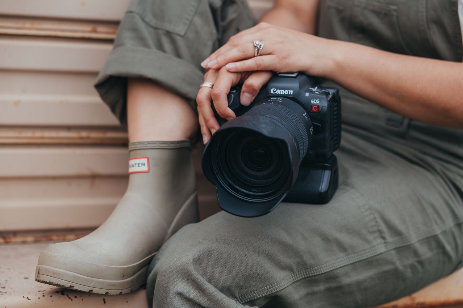 A Canon DSLR camera with telephoto lens sits next to beige rubber boots on wooden decking.