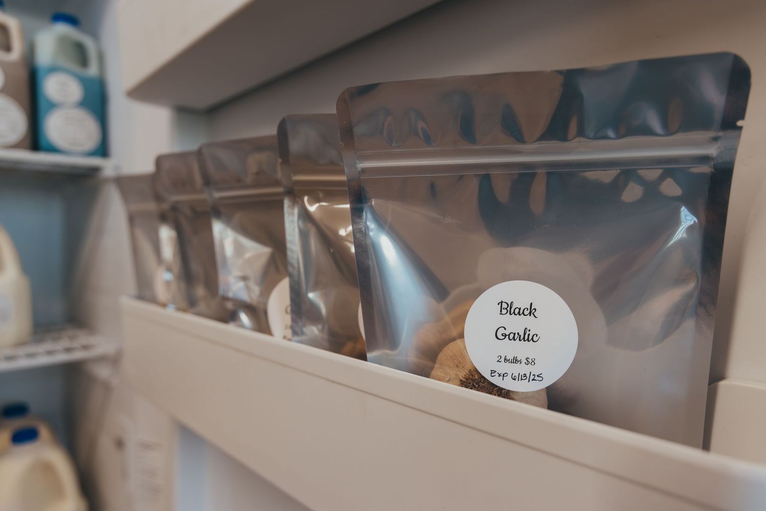Dark coffee bags with labels sit on white retail shelves against a light blue wall.