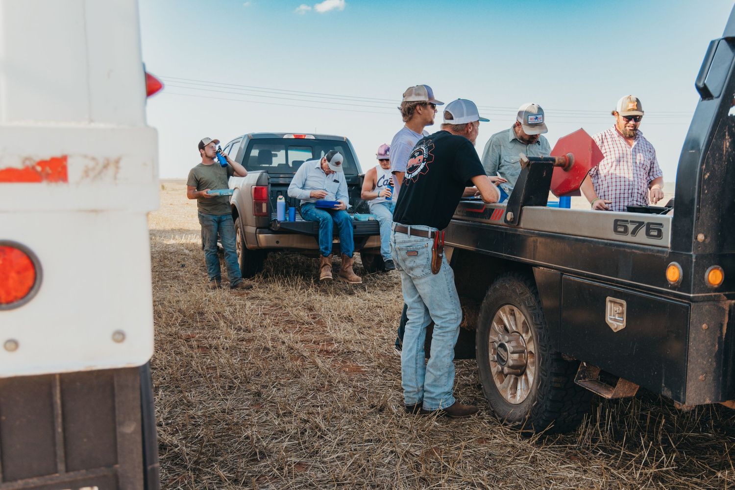 Trucks and vehicles parked in a row at a rural gathering, with attendees standing near their vehicles in a field.