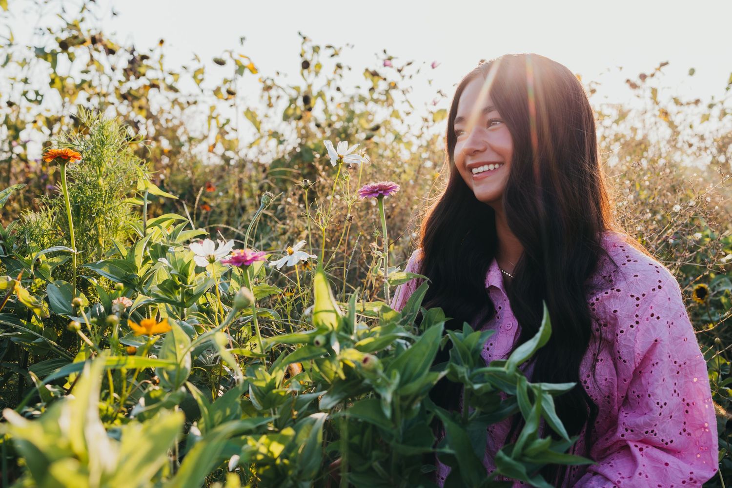 Woman in purple sweater laughs joyfully while sitting in an autumn garden with sunlight streaming through trees.