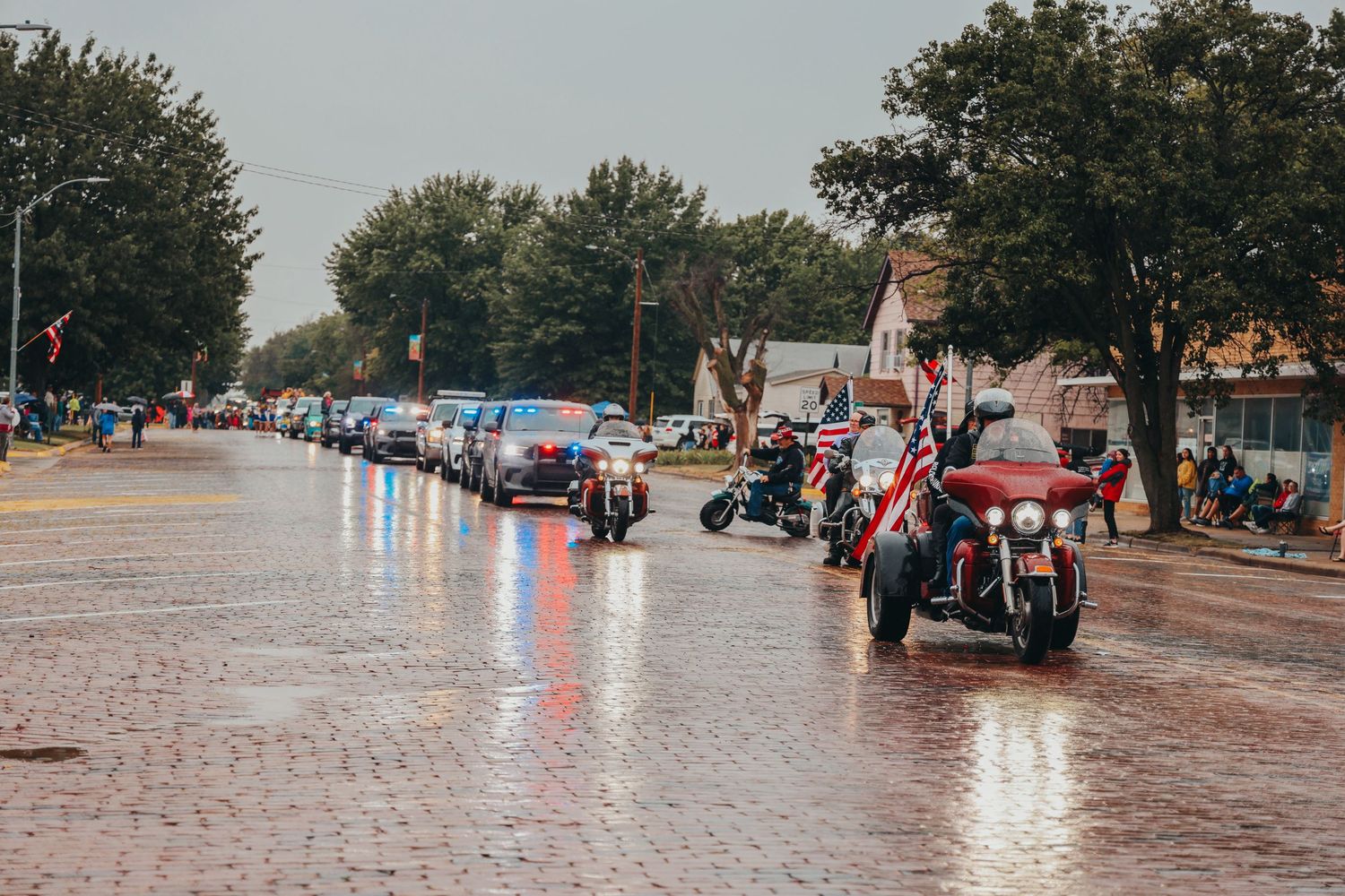 Line of motorcycles driving down wet street during parade.