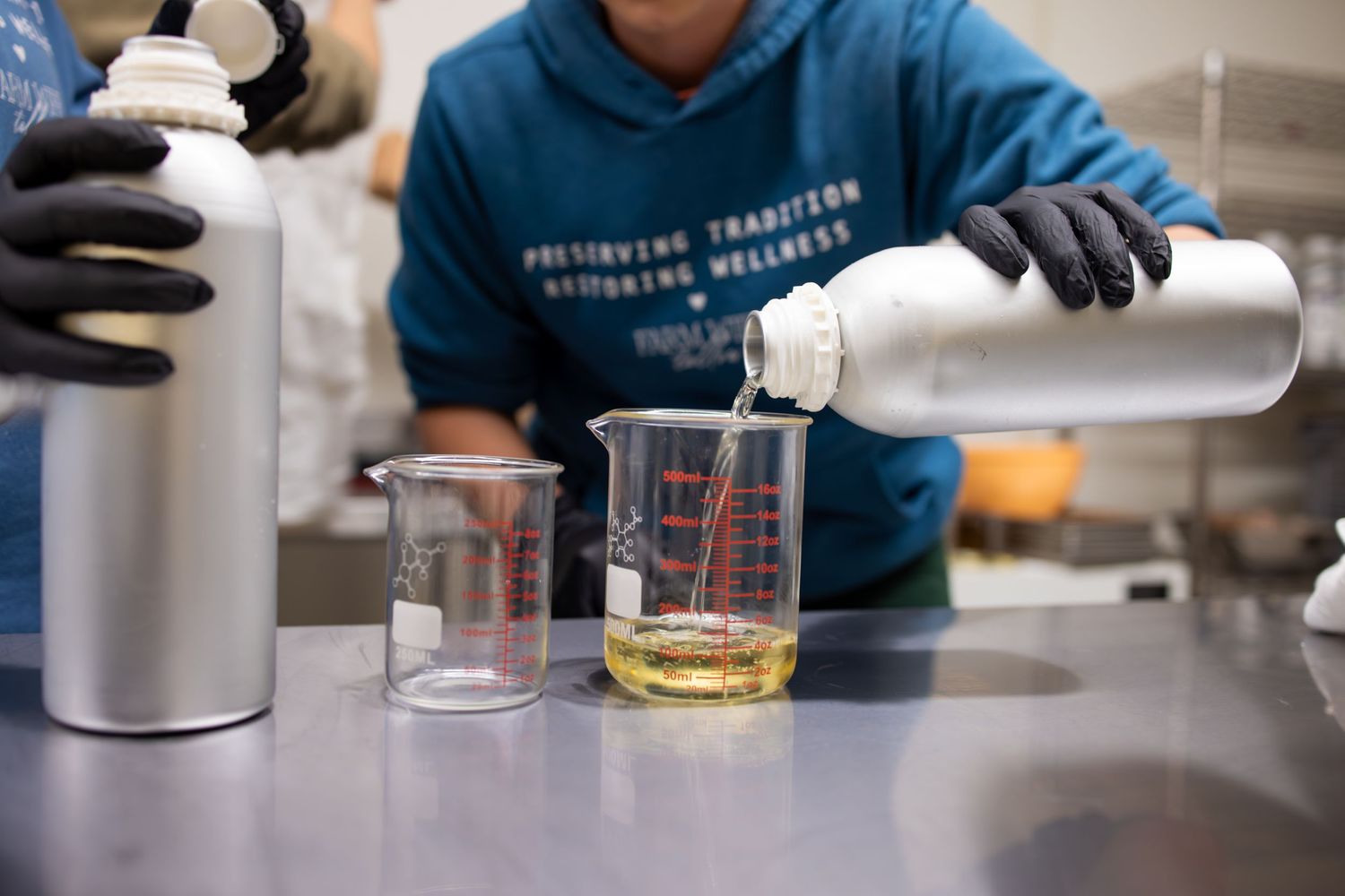Laboratory measuring with beakers and liquids being poured while wearing protective gloves.
