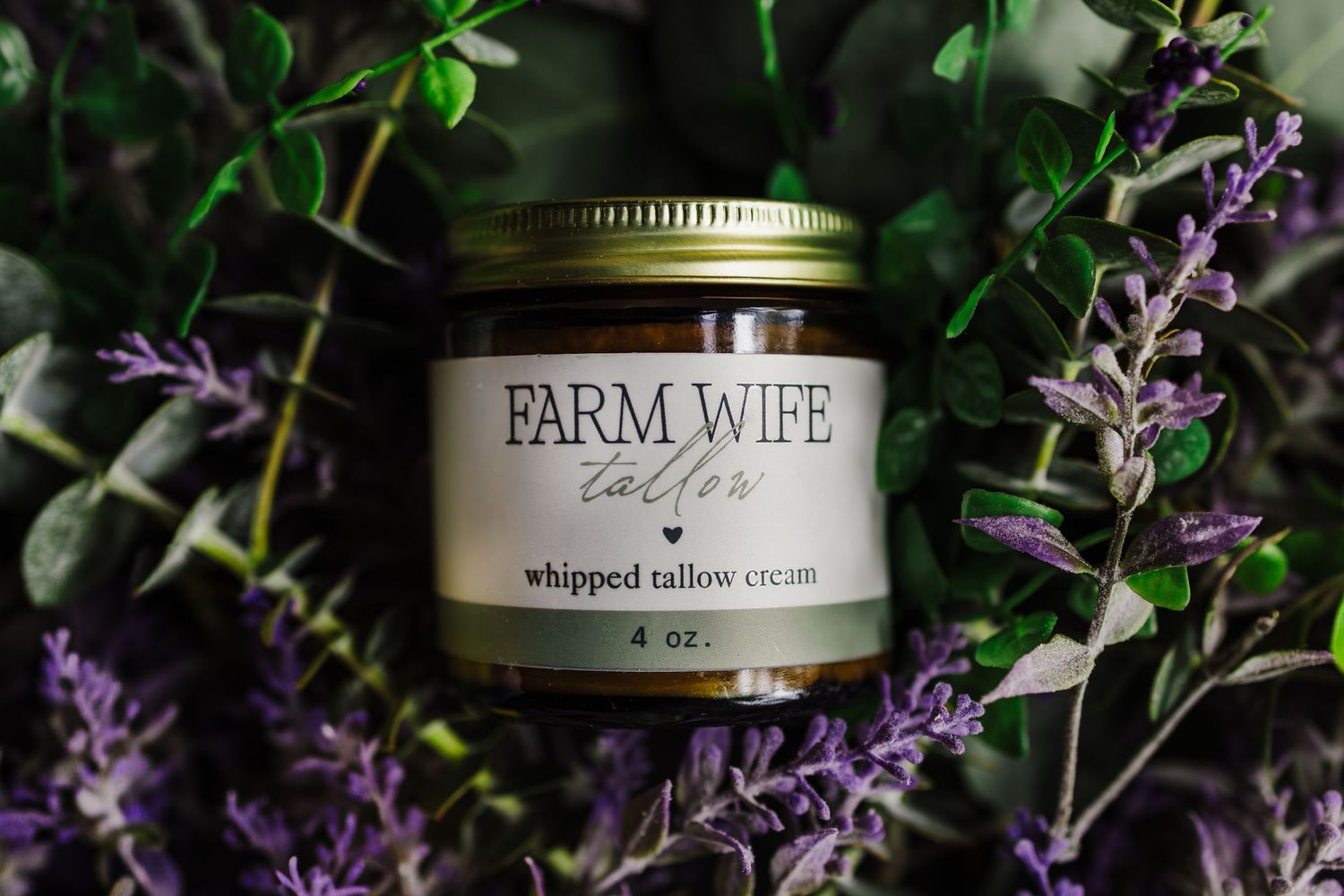 A Farm Wife whipped tallow cream jar nestled among purple lavender flowers and green foliage in soft lighting.