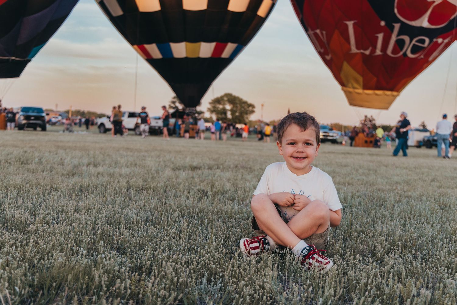 Hot air balloons at sunset with onlooker in foreground at outdoor festival.