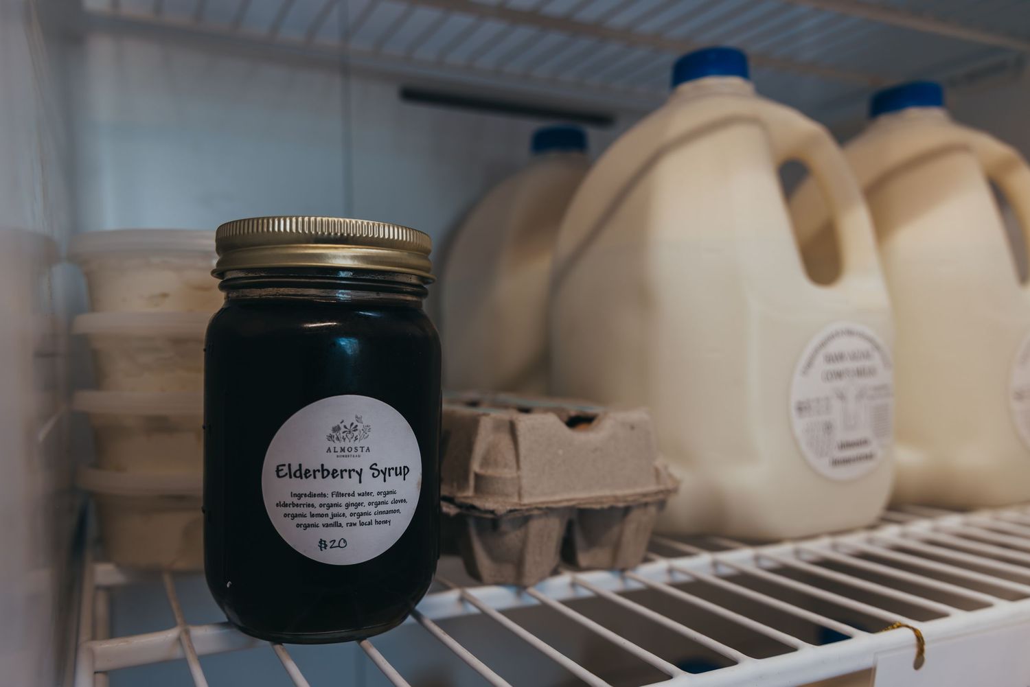 Glass mason jar with dark liquid sits in refrigerator shelf next to large white plastic containers.