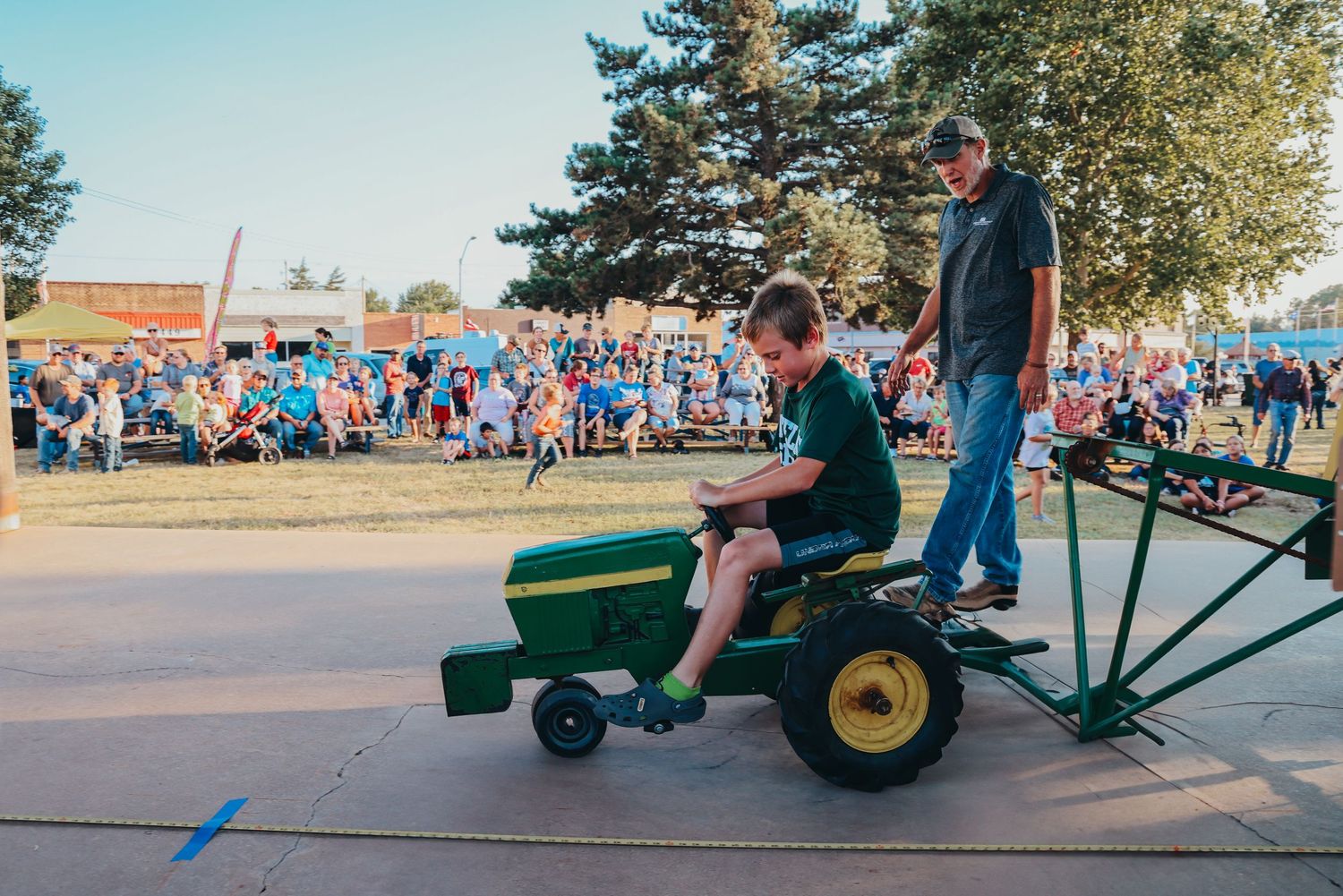 Child rides a green John Deere toy tractor during a community event.