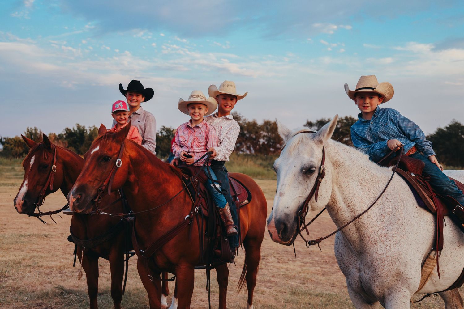 Family group riding horses together at sunset wearing western attire.
