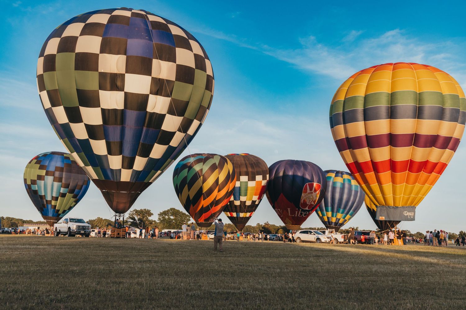 Multiple hot air balloons in various patterns prepare for launch at a festival.