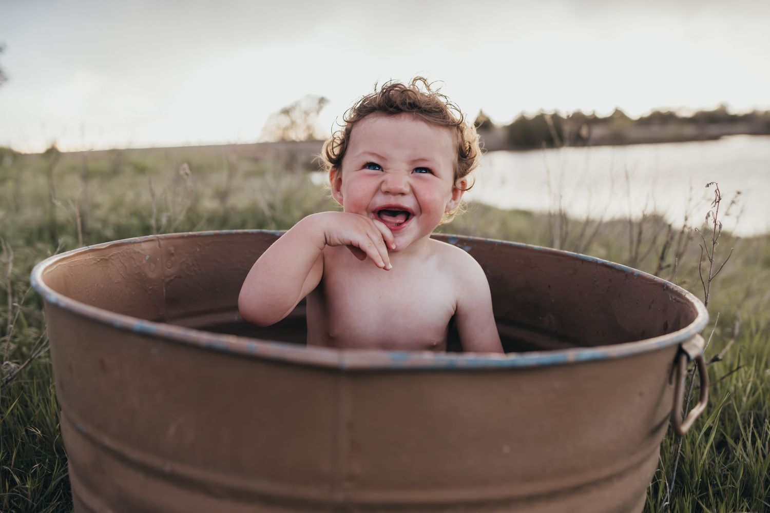 Joyful child playing in a rustic metal tub outdoors.