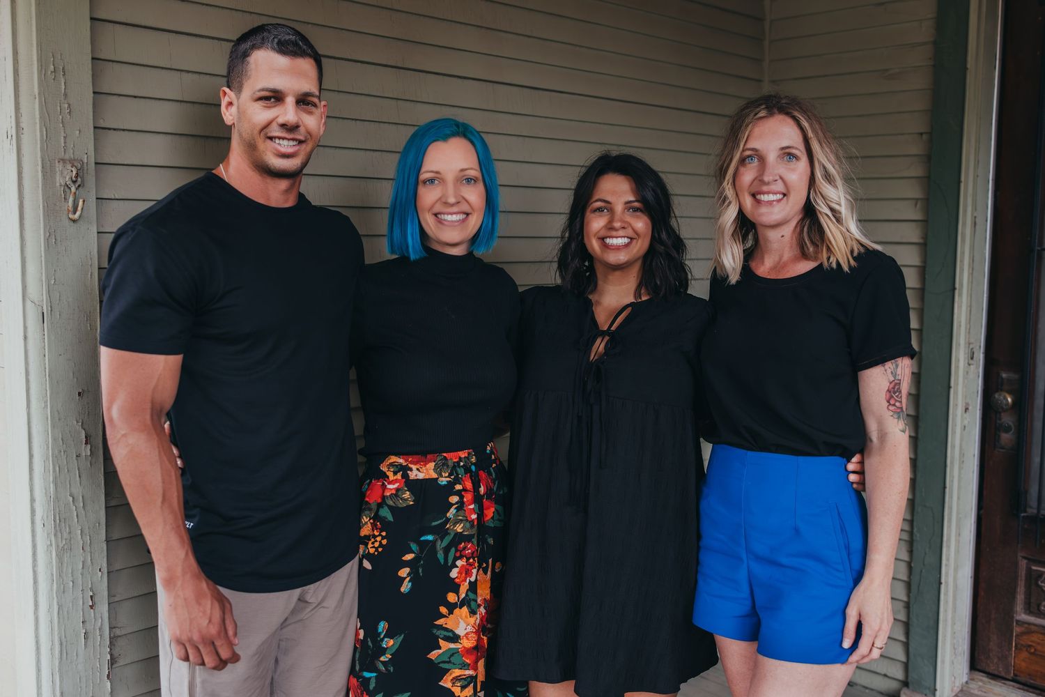 A group of four people wearing black and colorful outfits stand together on a porch.
