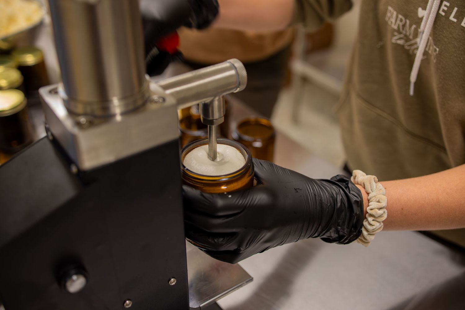 Hands in black gloves operating industrial equipment to fill product containers.