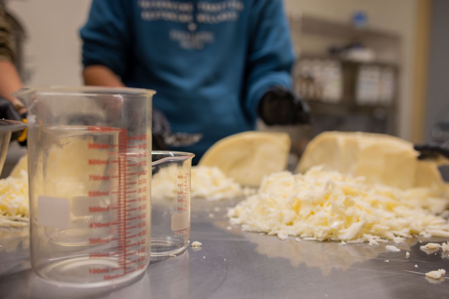 A measuring cup sits next to a pile of freshly grated cheese on a kitchen counter during food preparation.