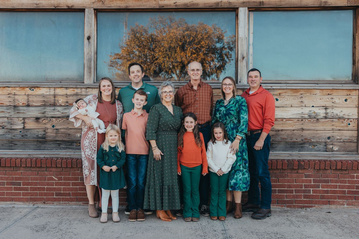 A group of people posed together outdoors against a rustic wooden and brick wall background.