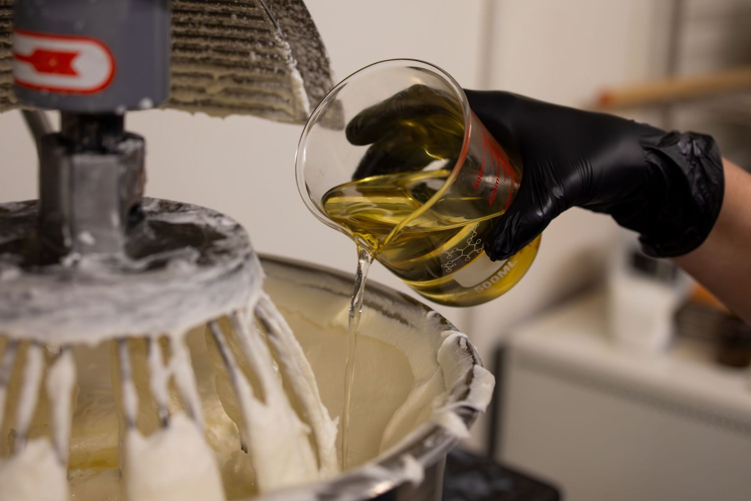 Amber liquid being poured from a glass beaker into industrial mixing equipment.