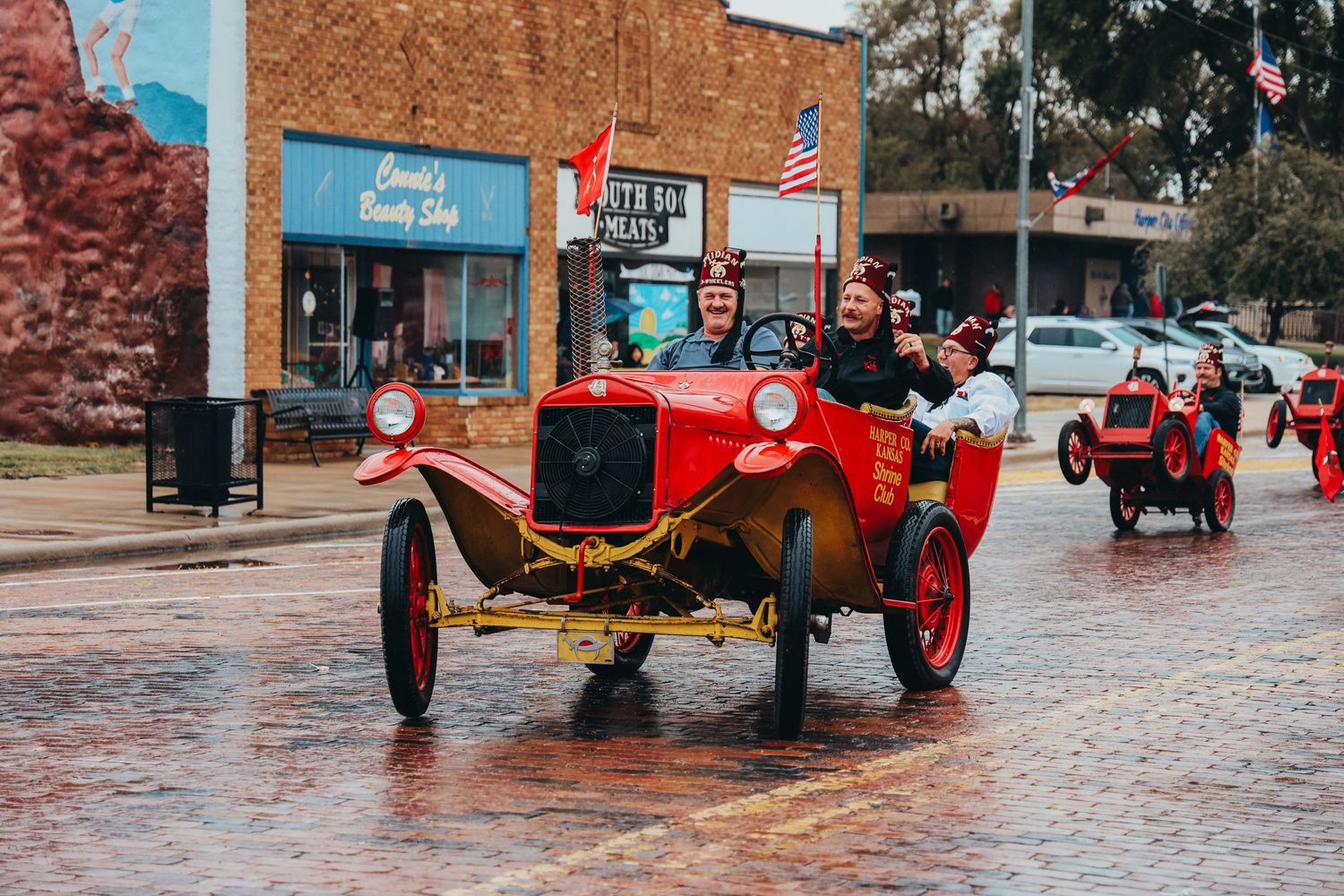 Classic red antique car driving on wet brick streets during a parade or festival.