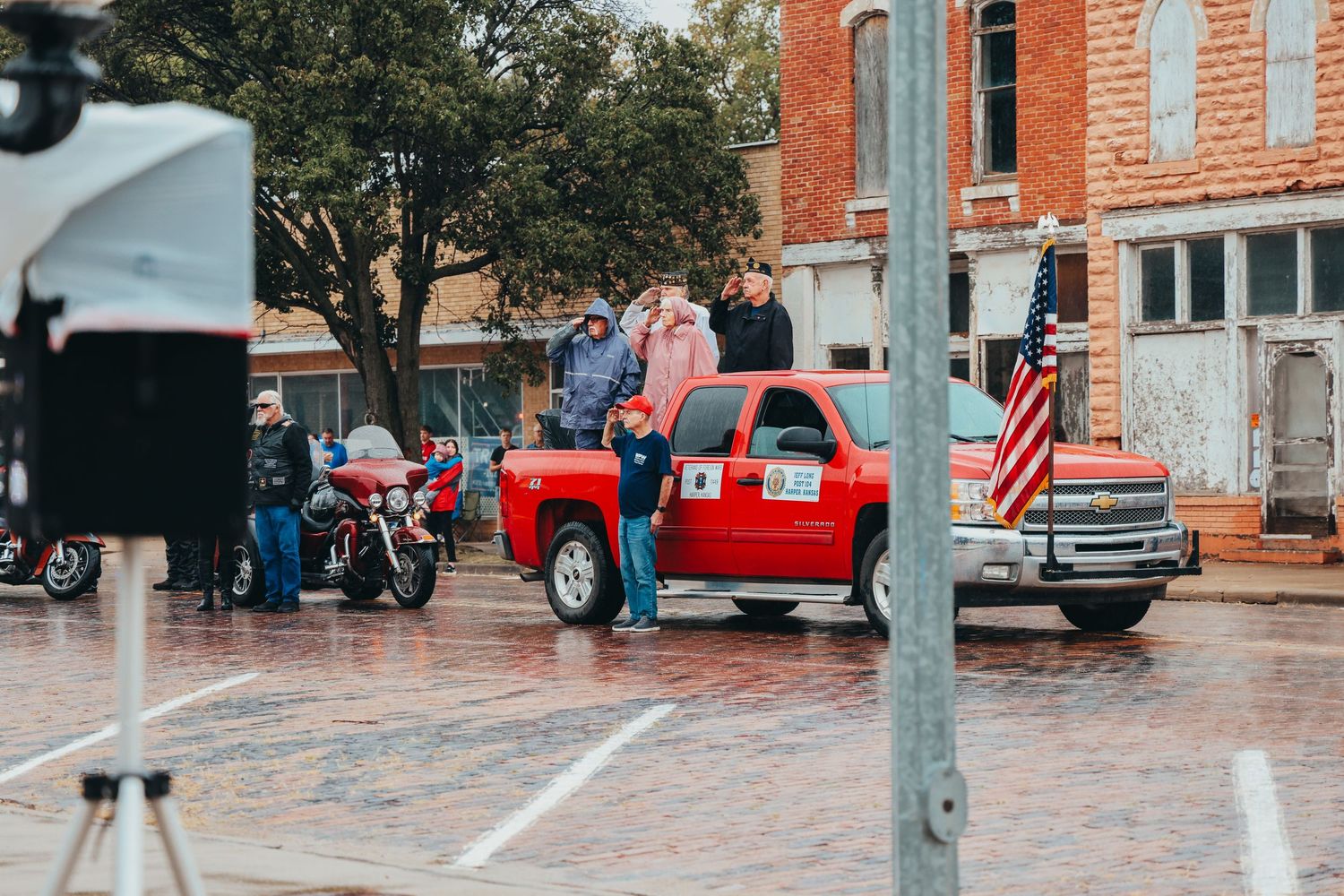 Red pickup truck parked on wet pavement during small town event.