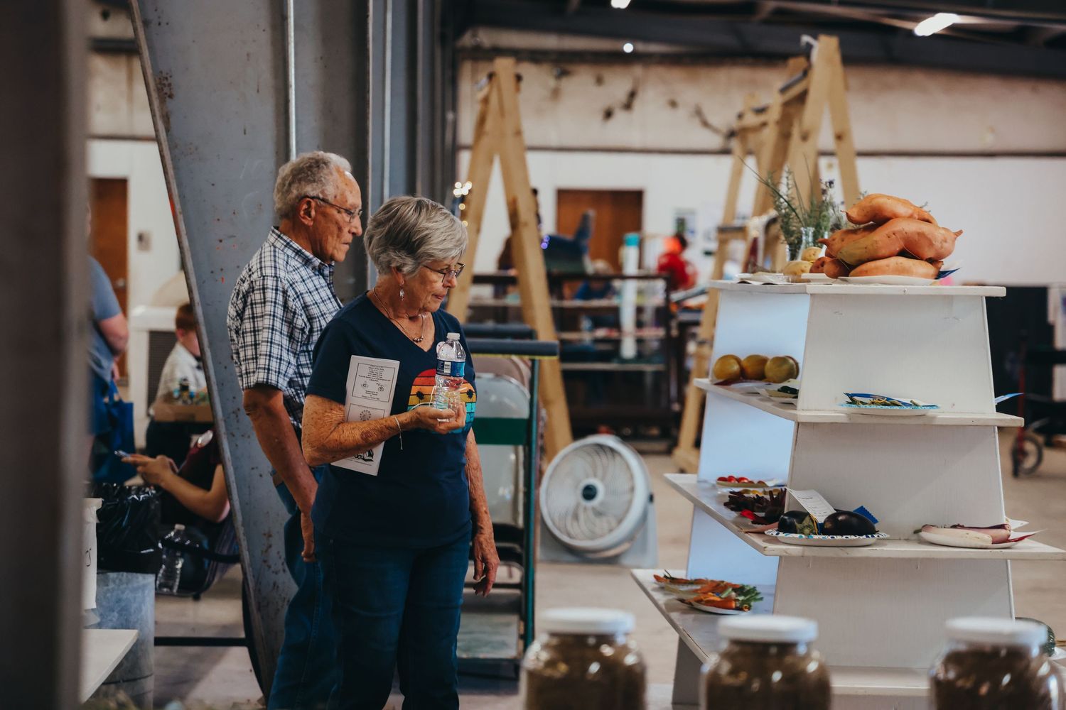 Shoppers browsing merchandise displays at an indoor market or craft fair.