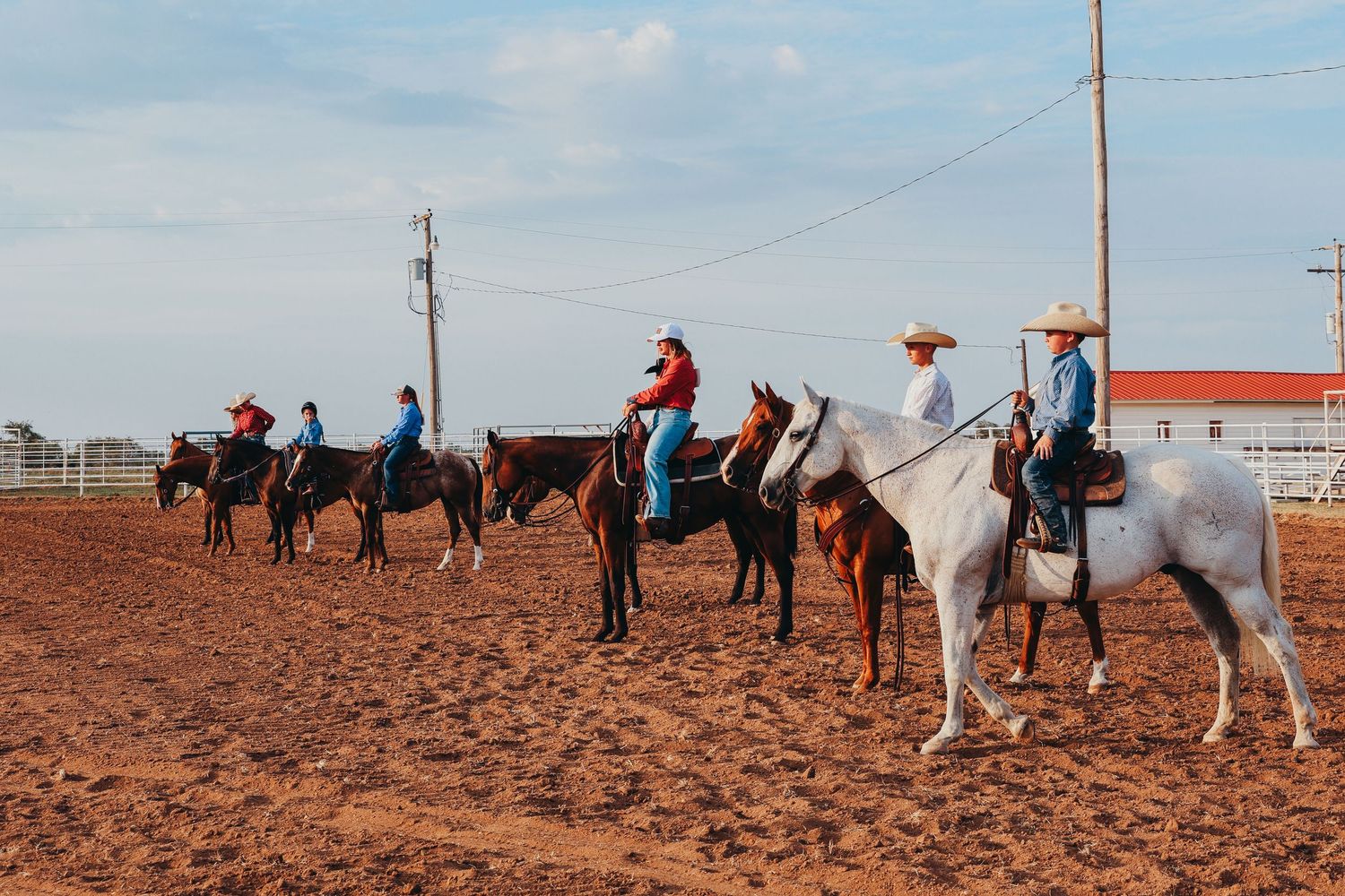 Line of riders on horseback in dusty rodeo arena.