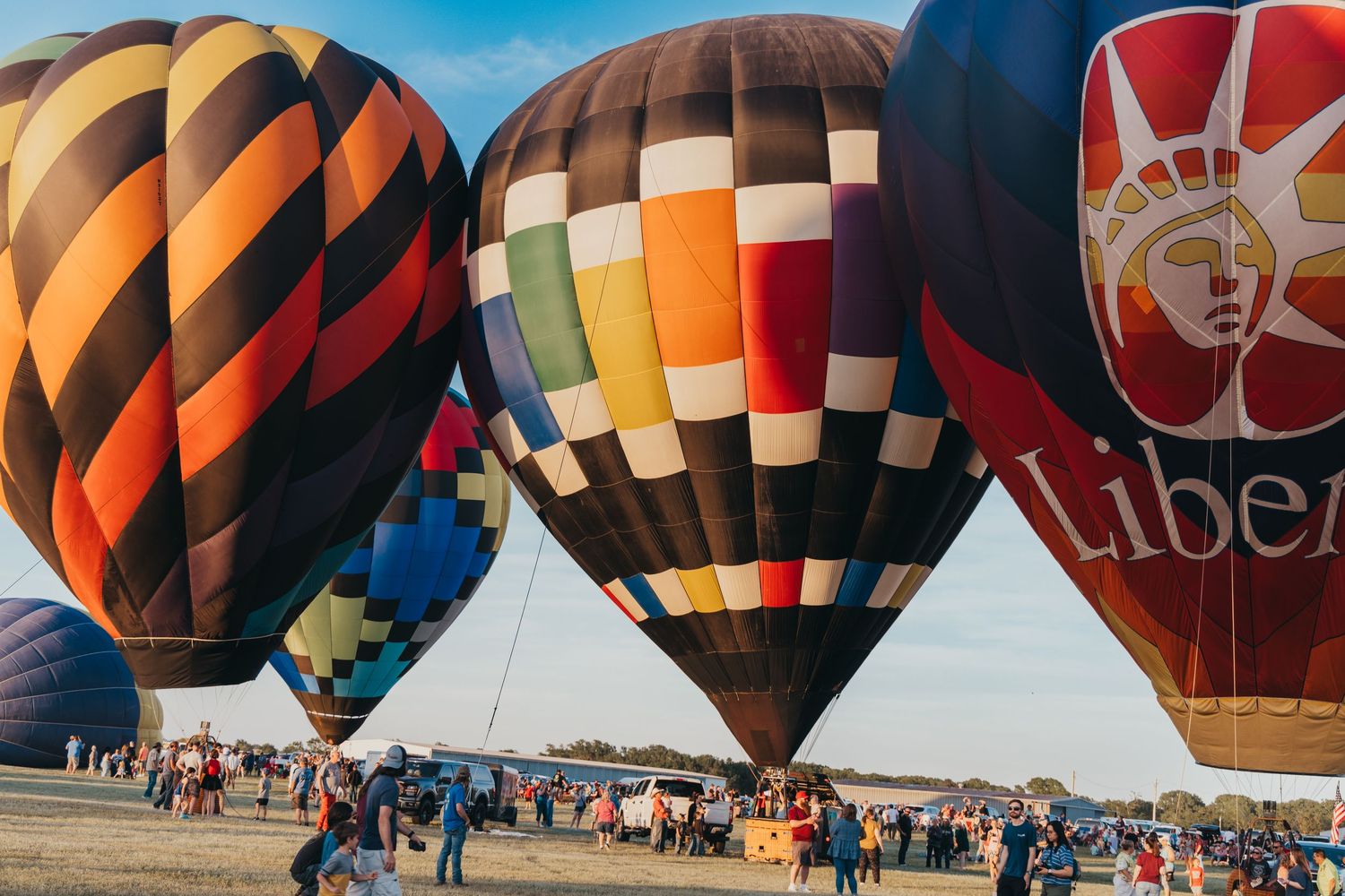 Multiple vibrant hot air balloons on display at a festival with crowds gathered below.