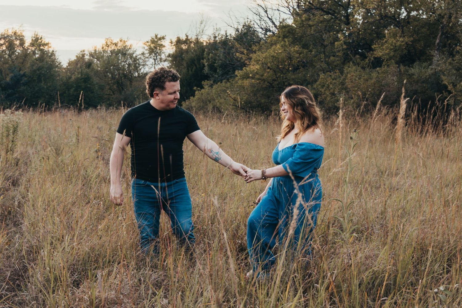 A couple in denim outfits playfully interacts in a golden autumn field during sunset.