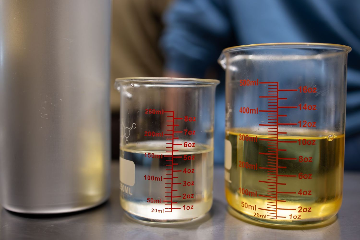Two glass beakers with measurements containing clear and amber liquids on laboratory surface.