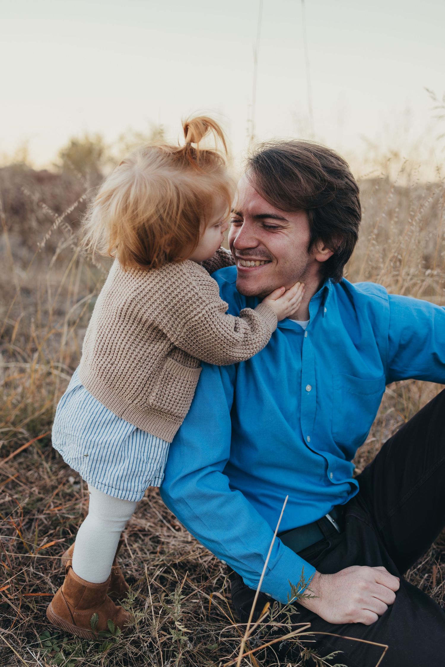 A tender moment between parent and child sharing a playful embrace in a sunlit field at golden hour.