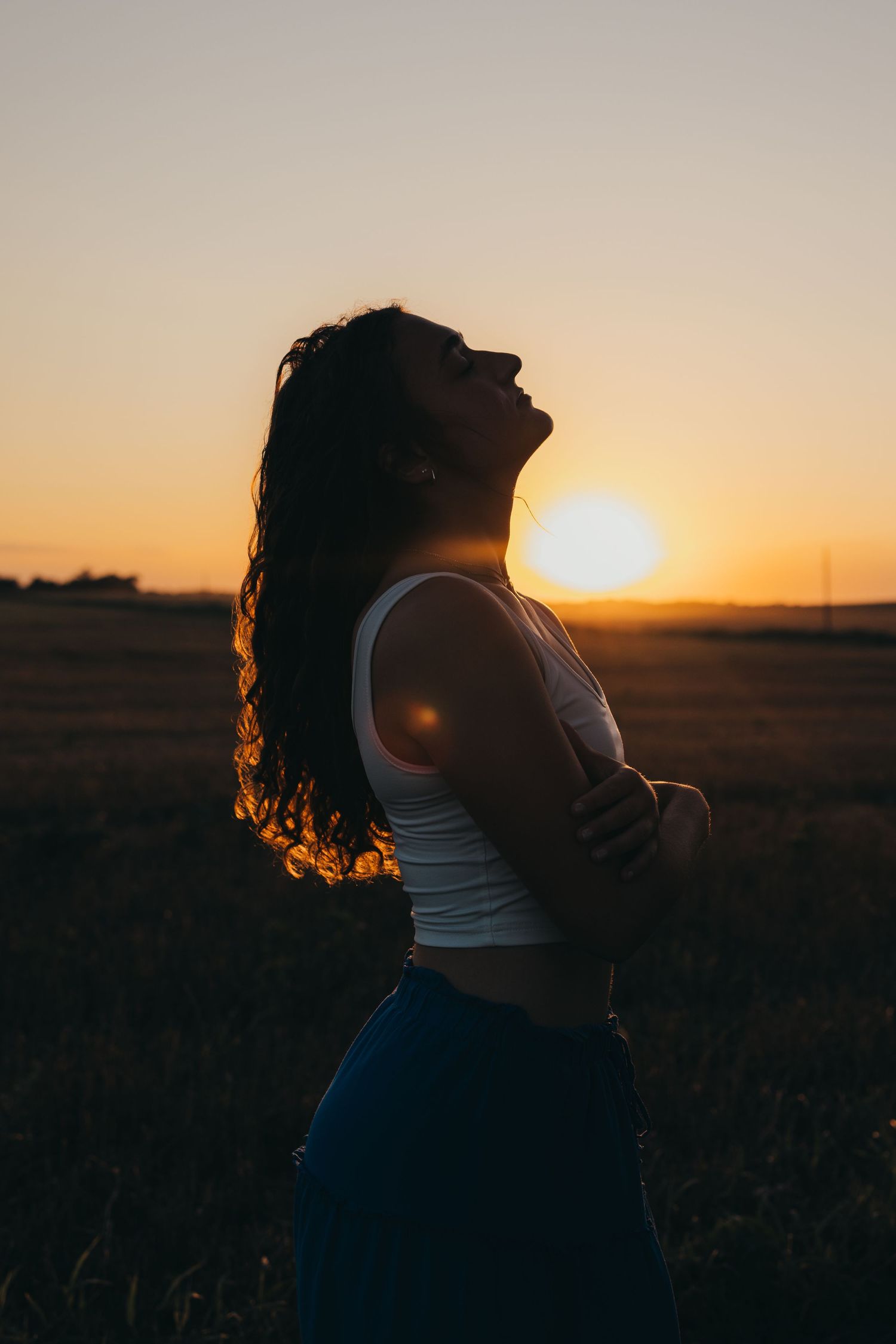 Silhouette of a person with long hair leaning back in a field during golden sunset.