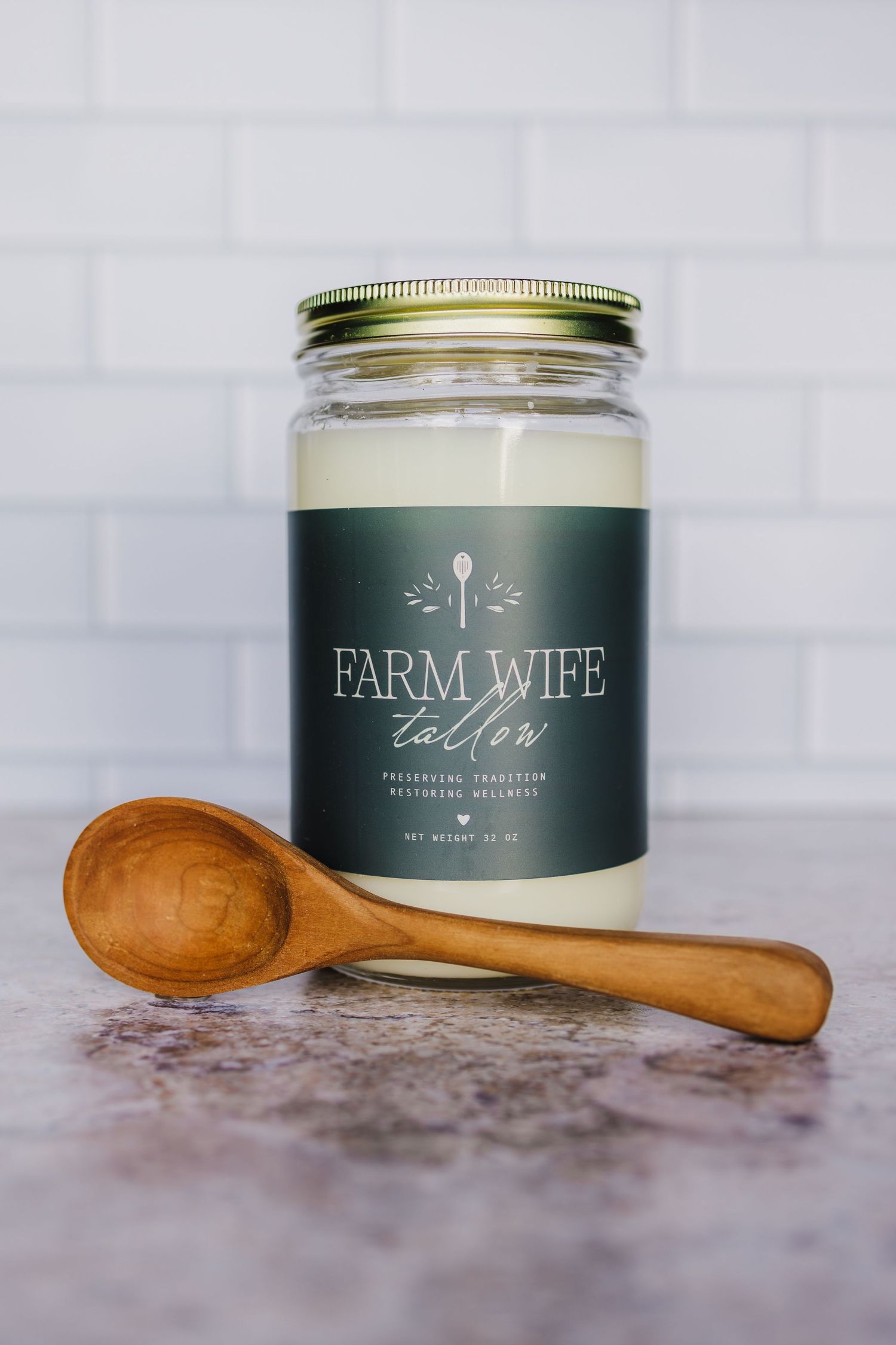 Green Farm Wife branded candle in glass jar with rustic wooden spoon on marble surface.
