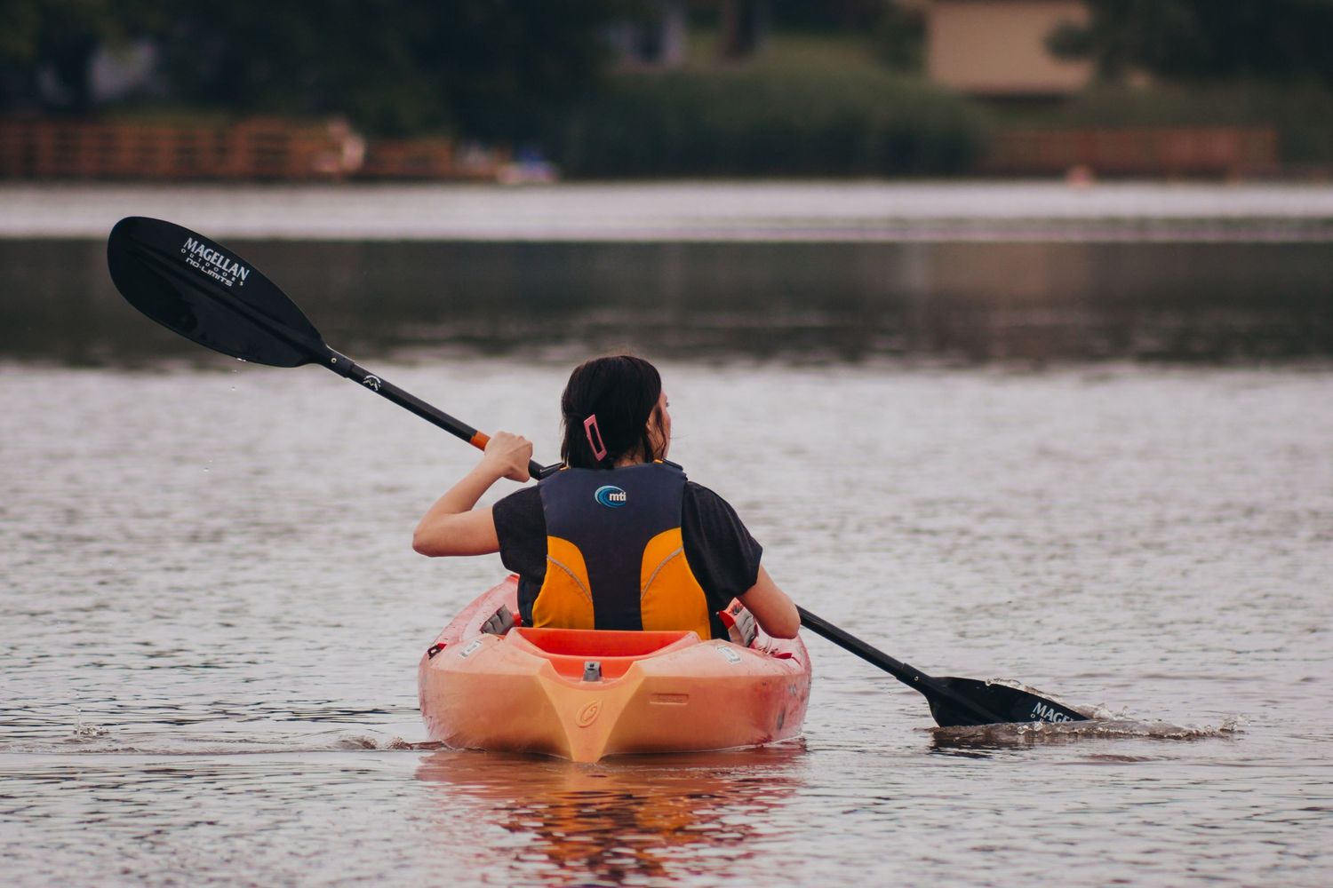 Person in orange life vest kayaking on calm water during cloudy weather.