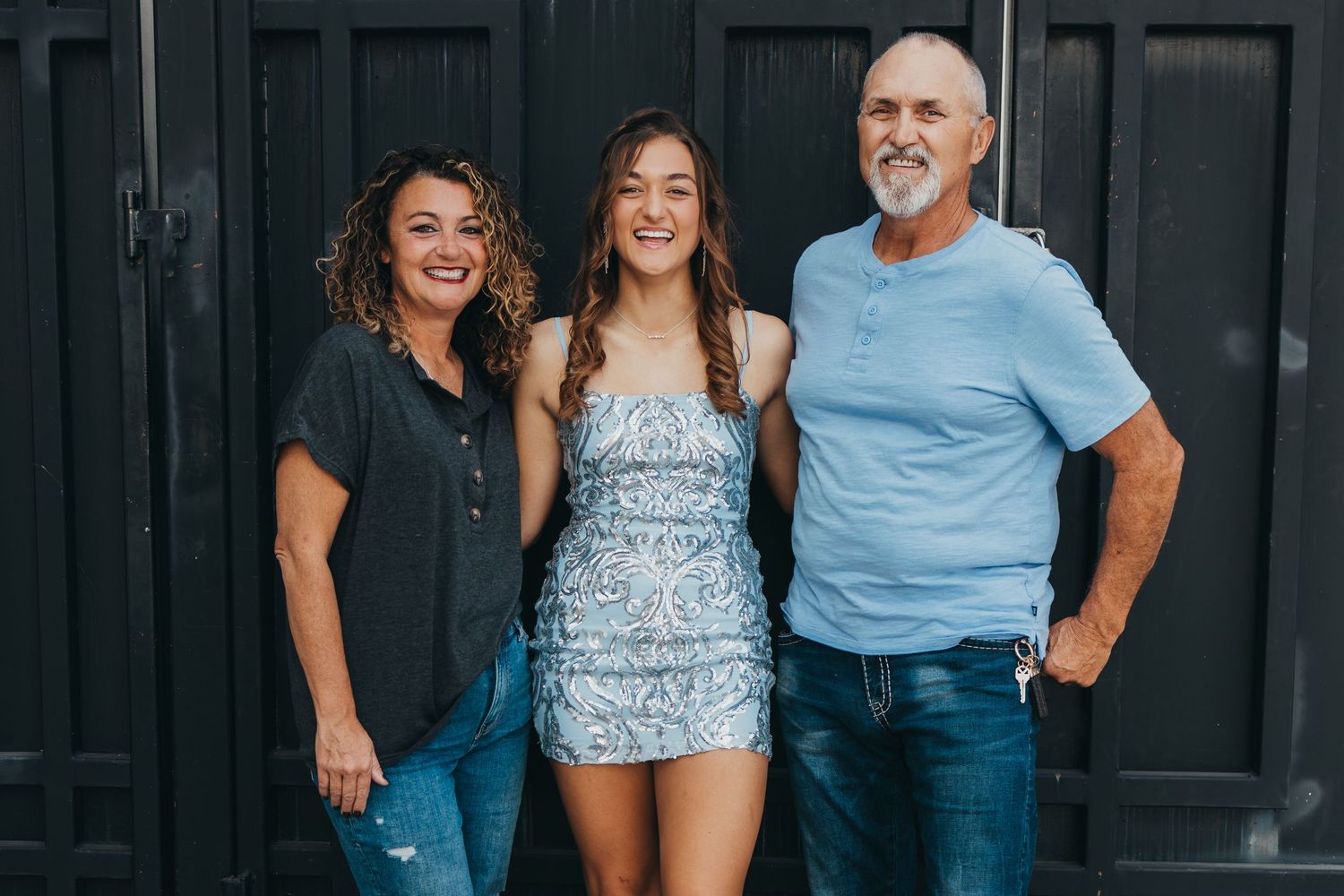 Three people pose together against a dark door background outdoors.