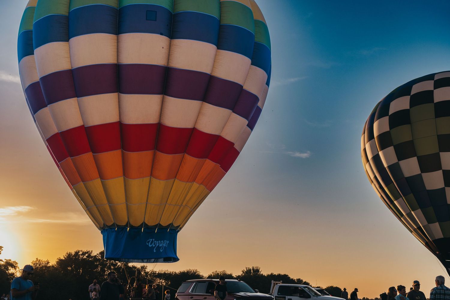 Striped hot air balloon in vibrant colors set against sunset sky with checkered balloon visible.