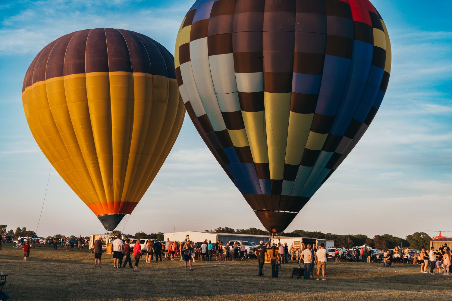 Two large hot air balloons preparing for takeoff with spectators gathered on a grassy field.
