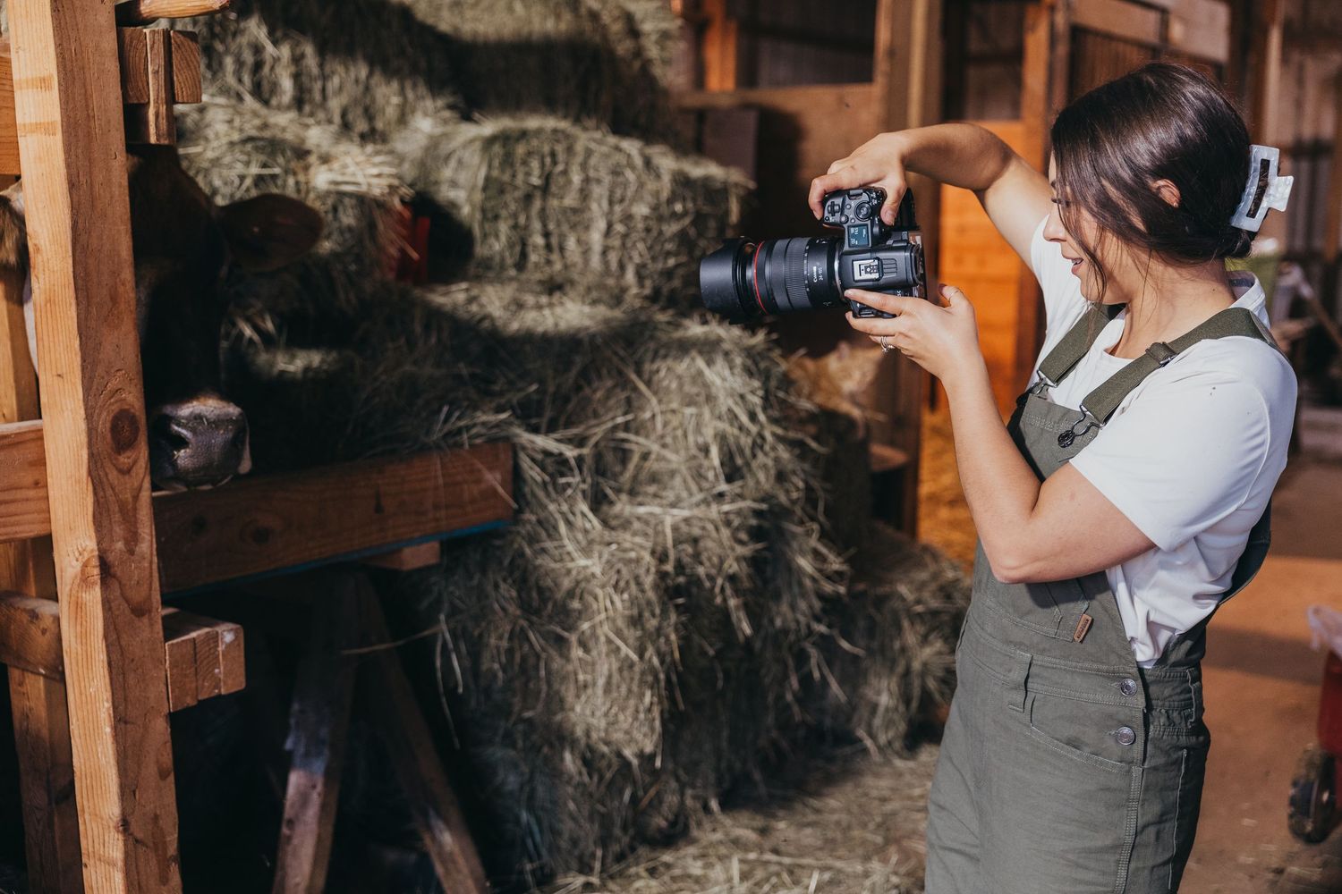 Photographer with professional camera taking pictures of hay bales inside rustic wooden barn.