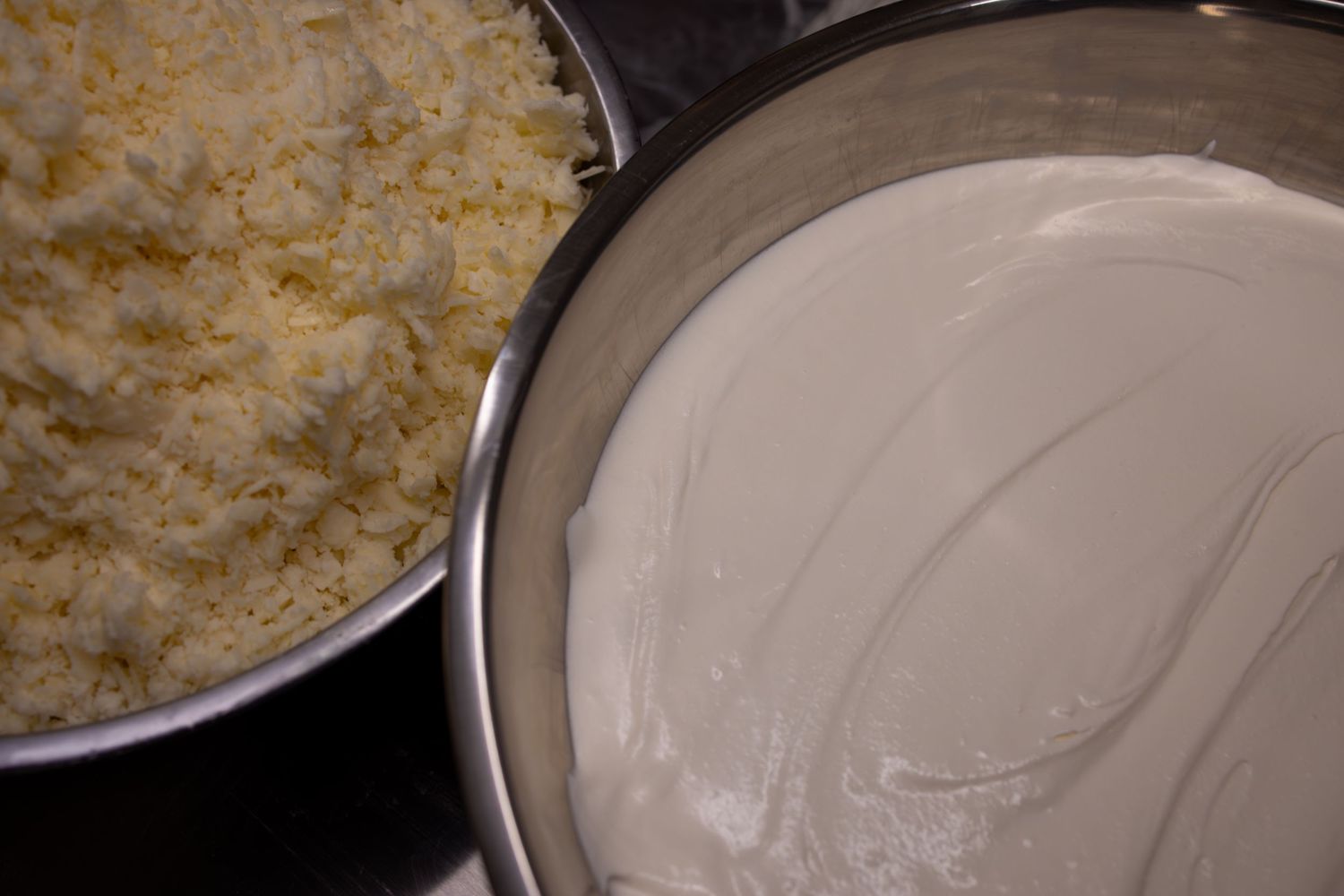 Two pans side by side with rice and creamy pink sauce in metal cookware on dark surface.
