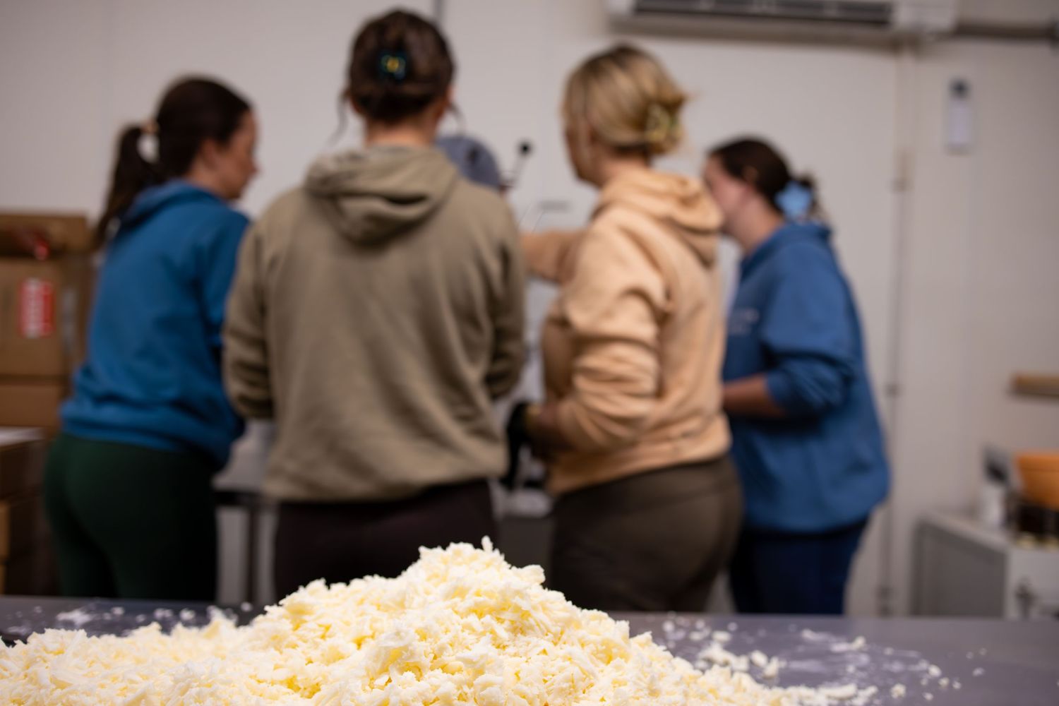 Pile of shredded cheese on a table with people working in the background.
