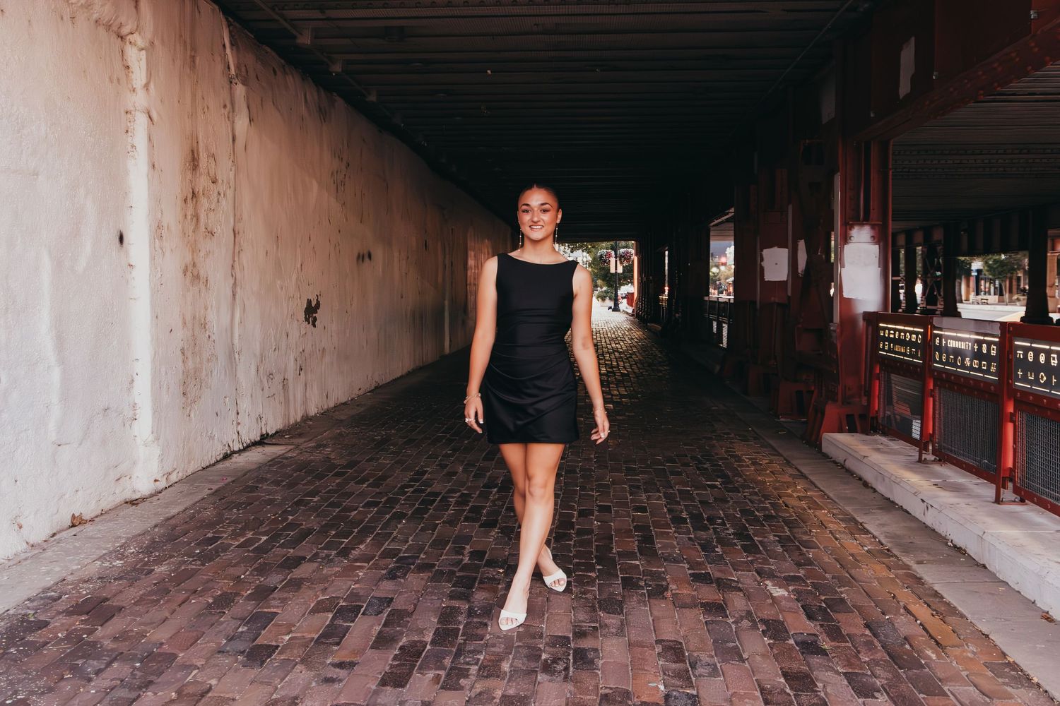 A person walks through a dimly lit historic brick tunnel with repeating archways and wooden floors.