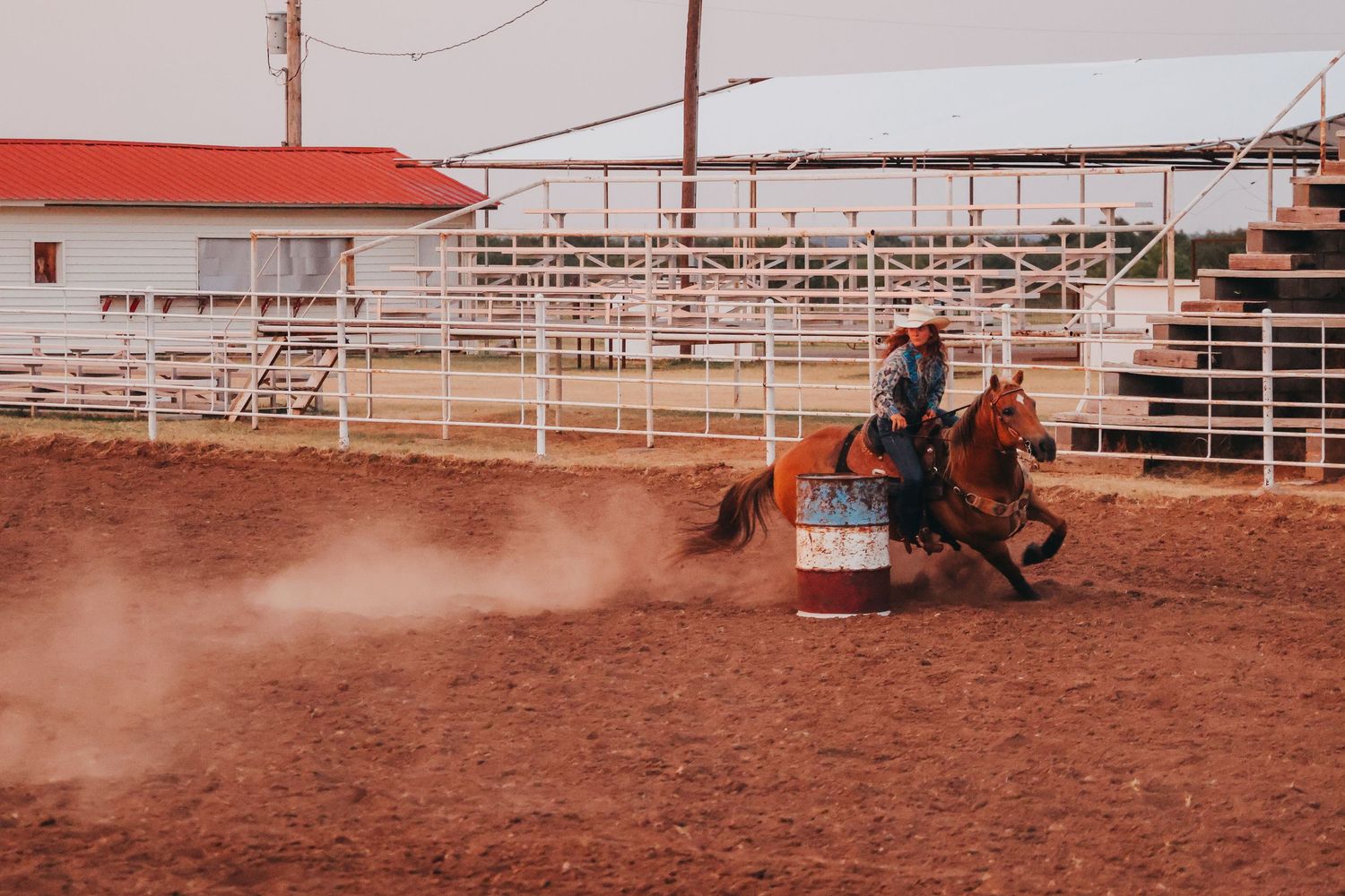 Barrel racing contestant kicks up dust in a rodeo arena during competition.