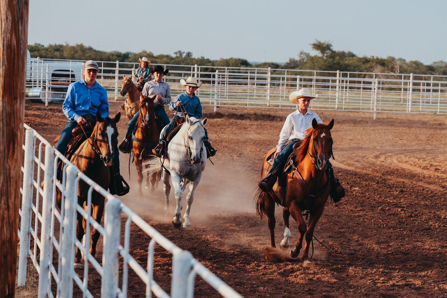 Group of riders on horseback kicking up dust in rodeo arena.