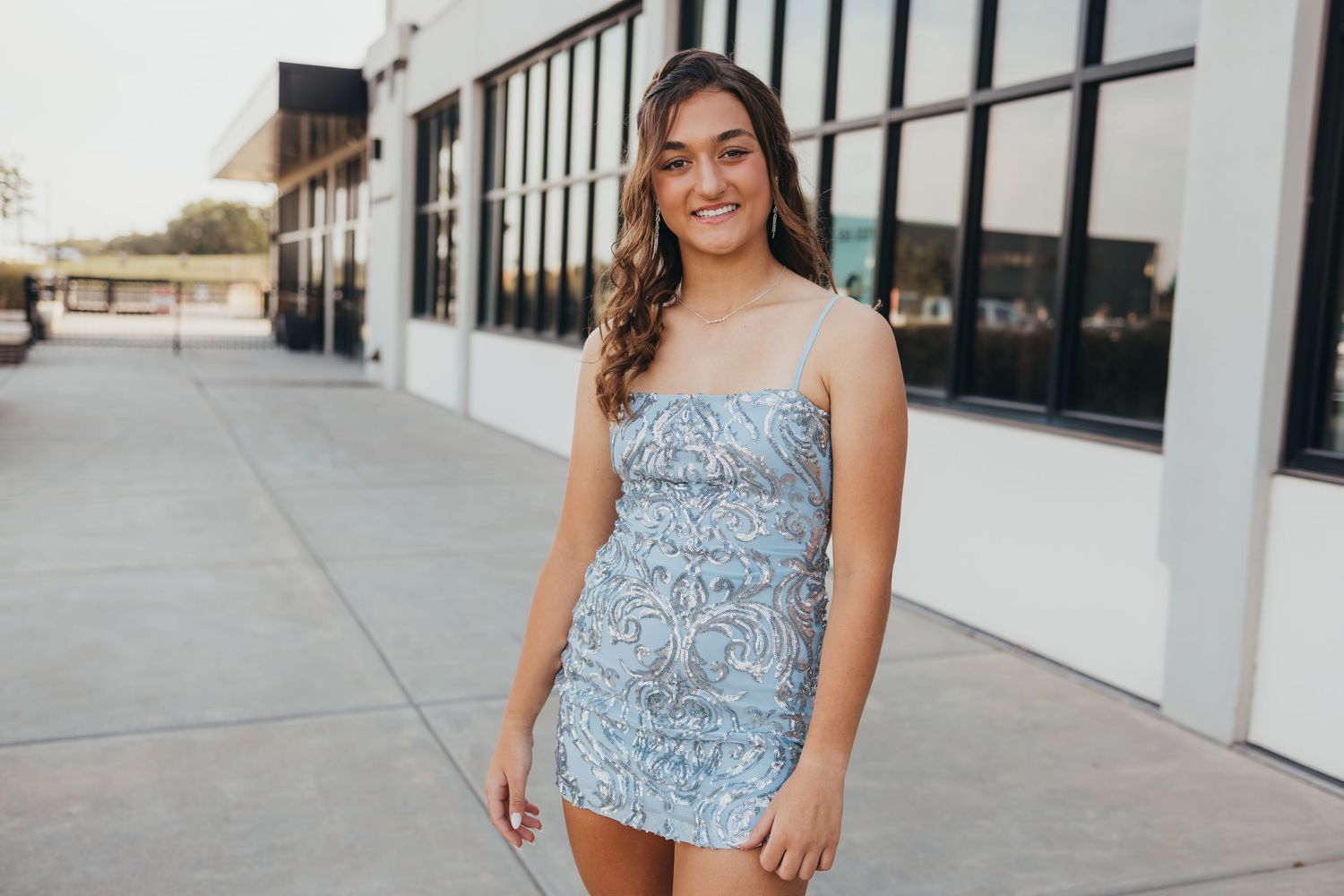 Portrait of someone in a light blue patterned mini dress standing outside a modern building.