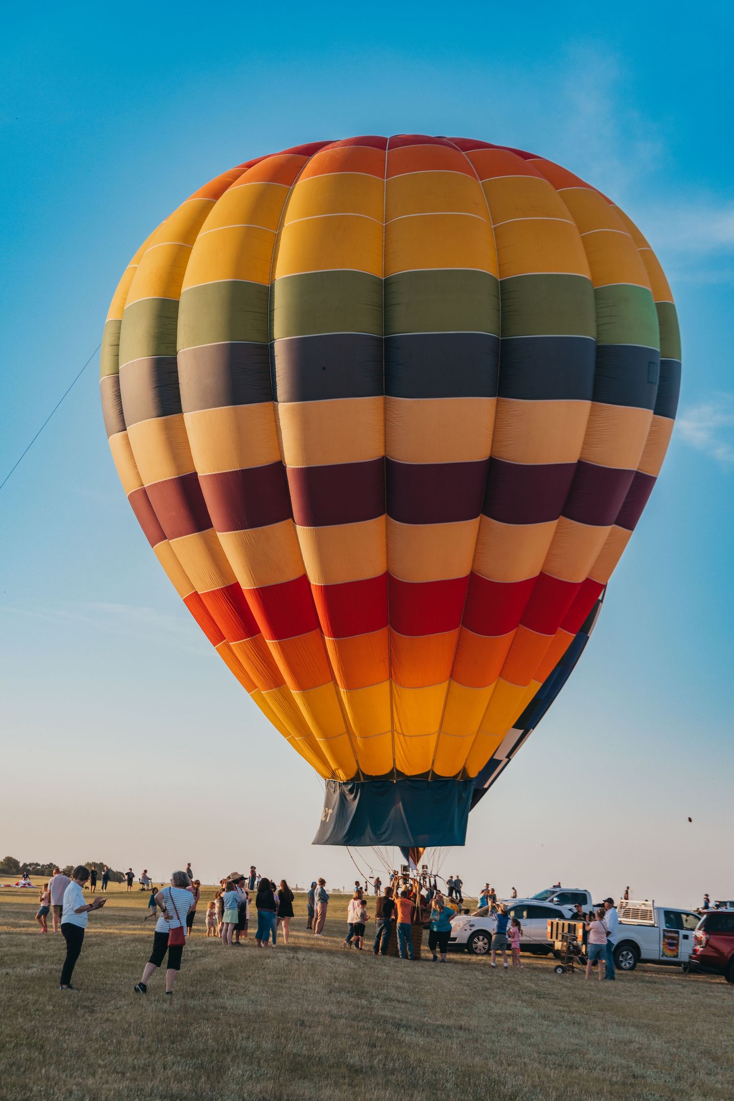 Colorful hot air balloon with orange and brown stripes being prepared for launch as spectators gather around.