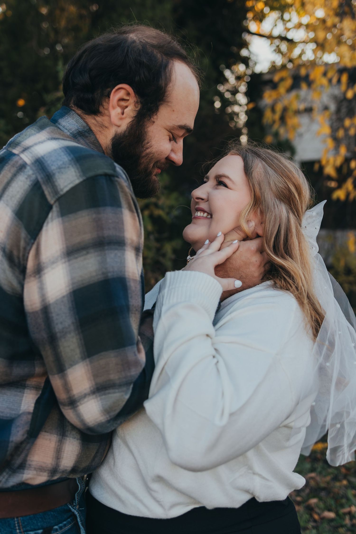 A couple shares tender moments outdoors in autumn, with golden leaves visible in the background.