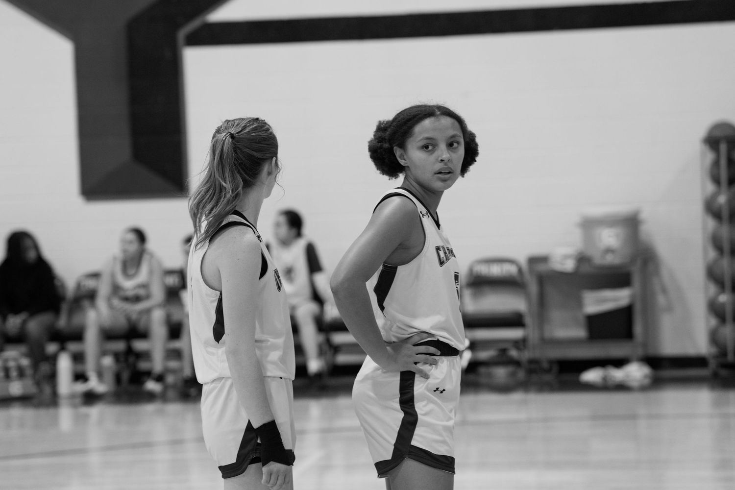 Two basketball players in white uniforms stand on the court during a black and white game moment.