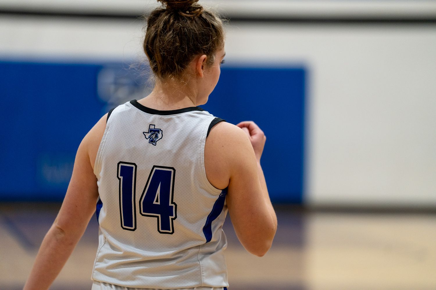 Basketball player in white jersey with blue numbers makes a jump shot during competitive game action.