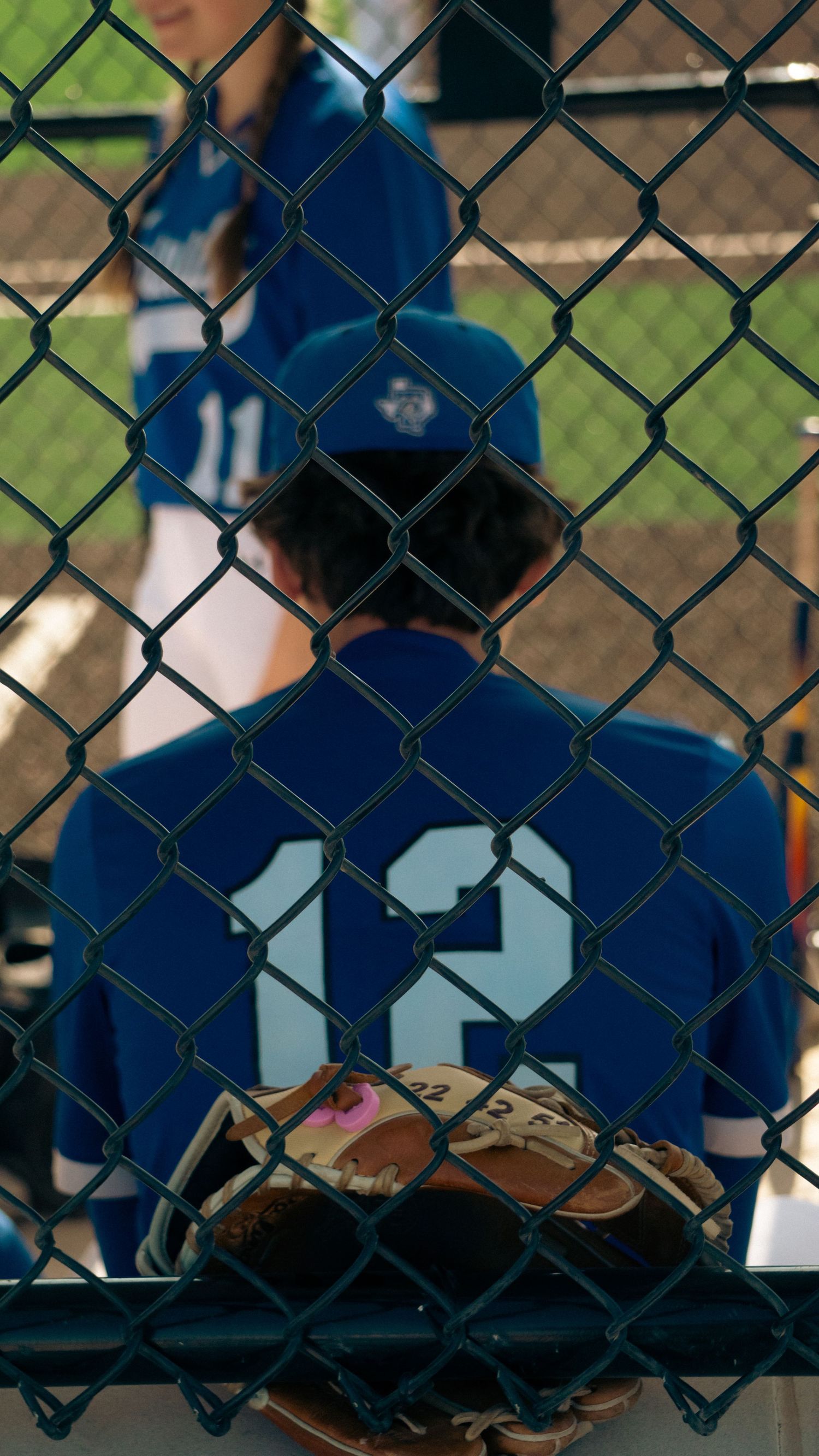 Baseball player in blue jersey number 12 viewed through chain link fence.
