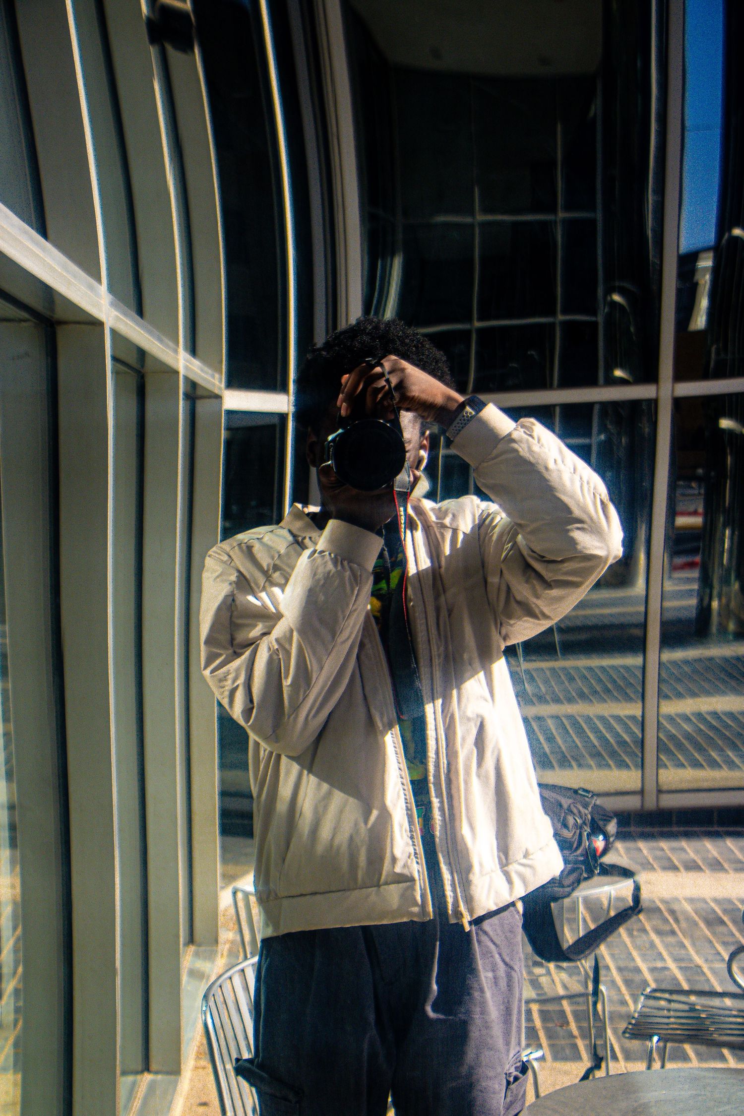 A photographer wearing a light jacket takes pictures against a modern glass building exterior.