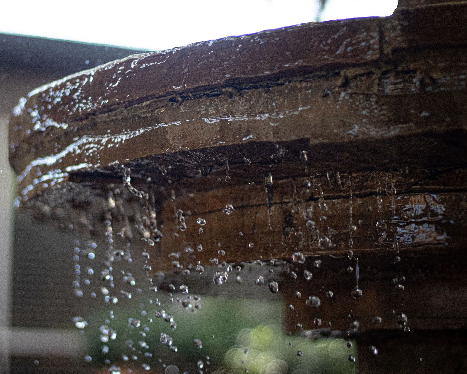 Water droplets falling from a wooden surface creating a natural stream effect.