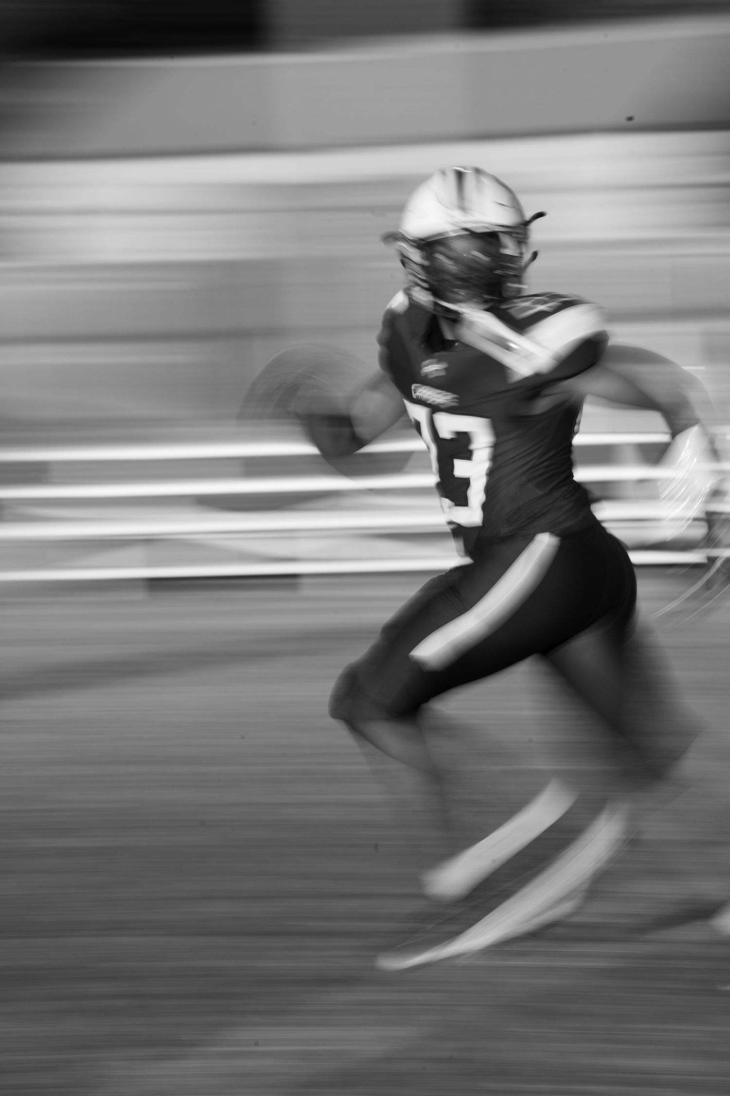 Black and white motion blur photograph of a football player running at high speed during a game.